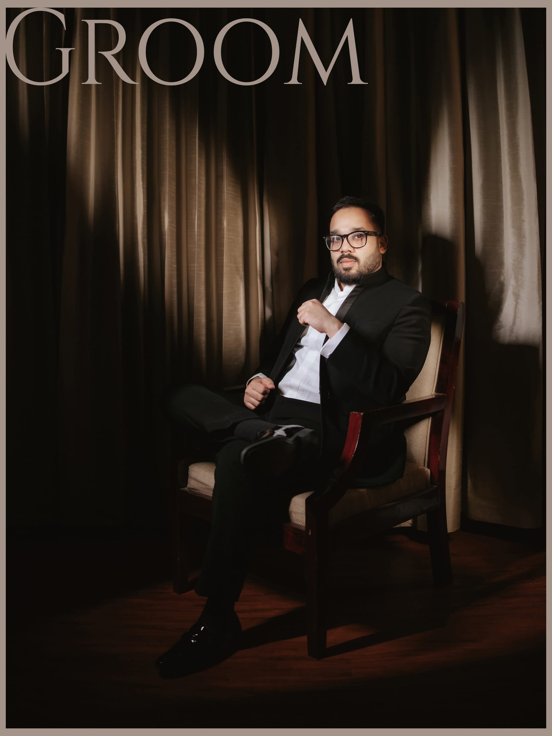The groom seated in a dark room, fixing his bow tie