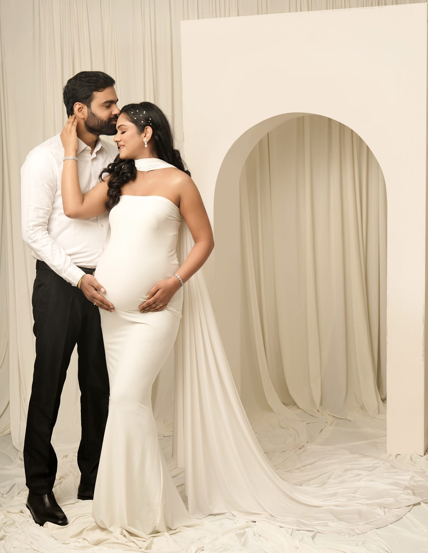 An expectant couple photographed in a cream studio set
