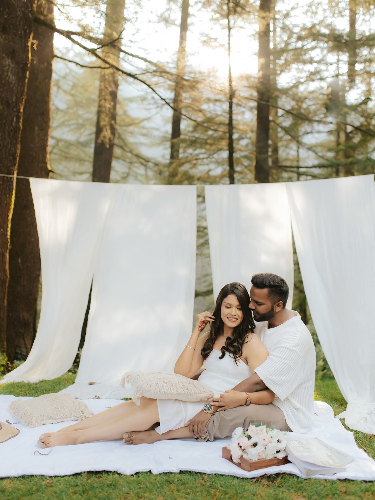 A couple on a picnic blanket among tall pines in low afternoon sun