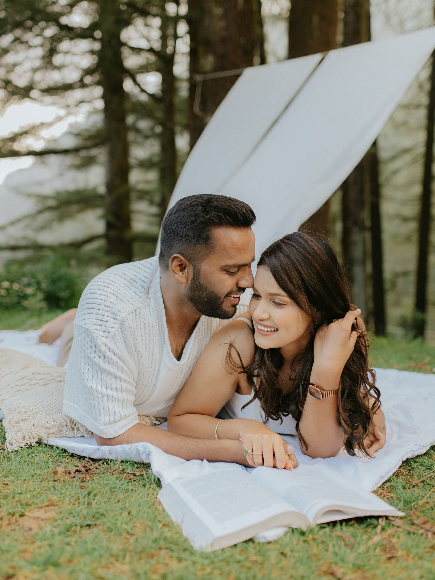 A couple lying on a blanket in a pine forest, laughing together