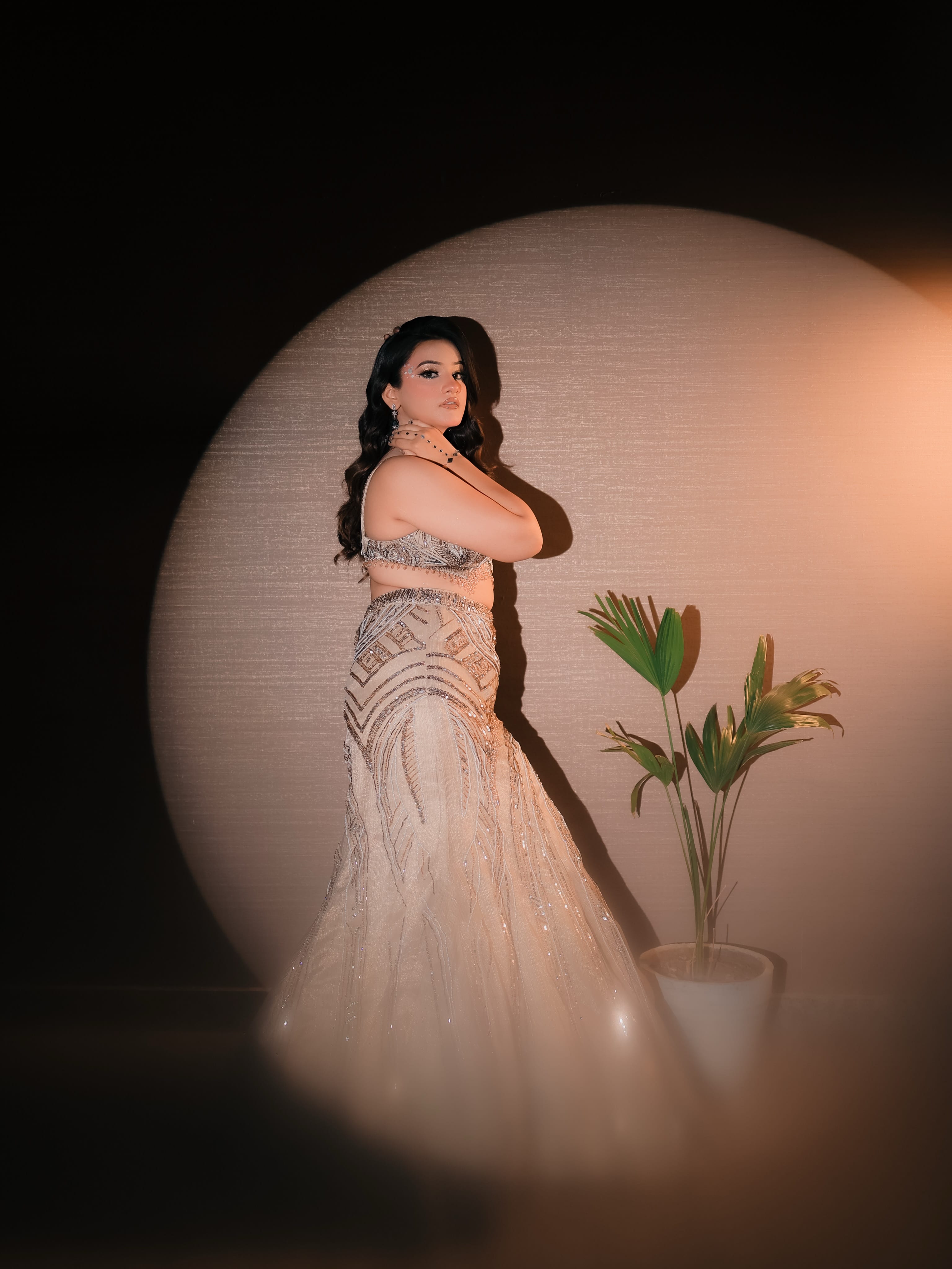 A bride in a beaded gown lit by a single spotlight against a warm wall