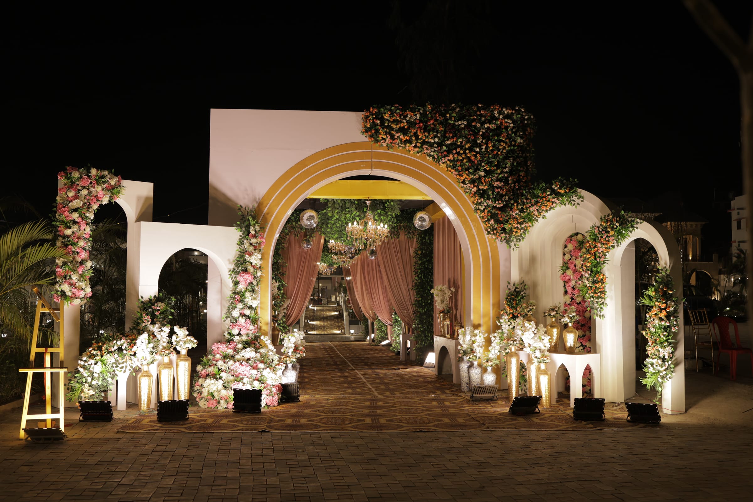 A floral entrance arch lit at night, leading into the venue