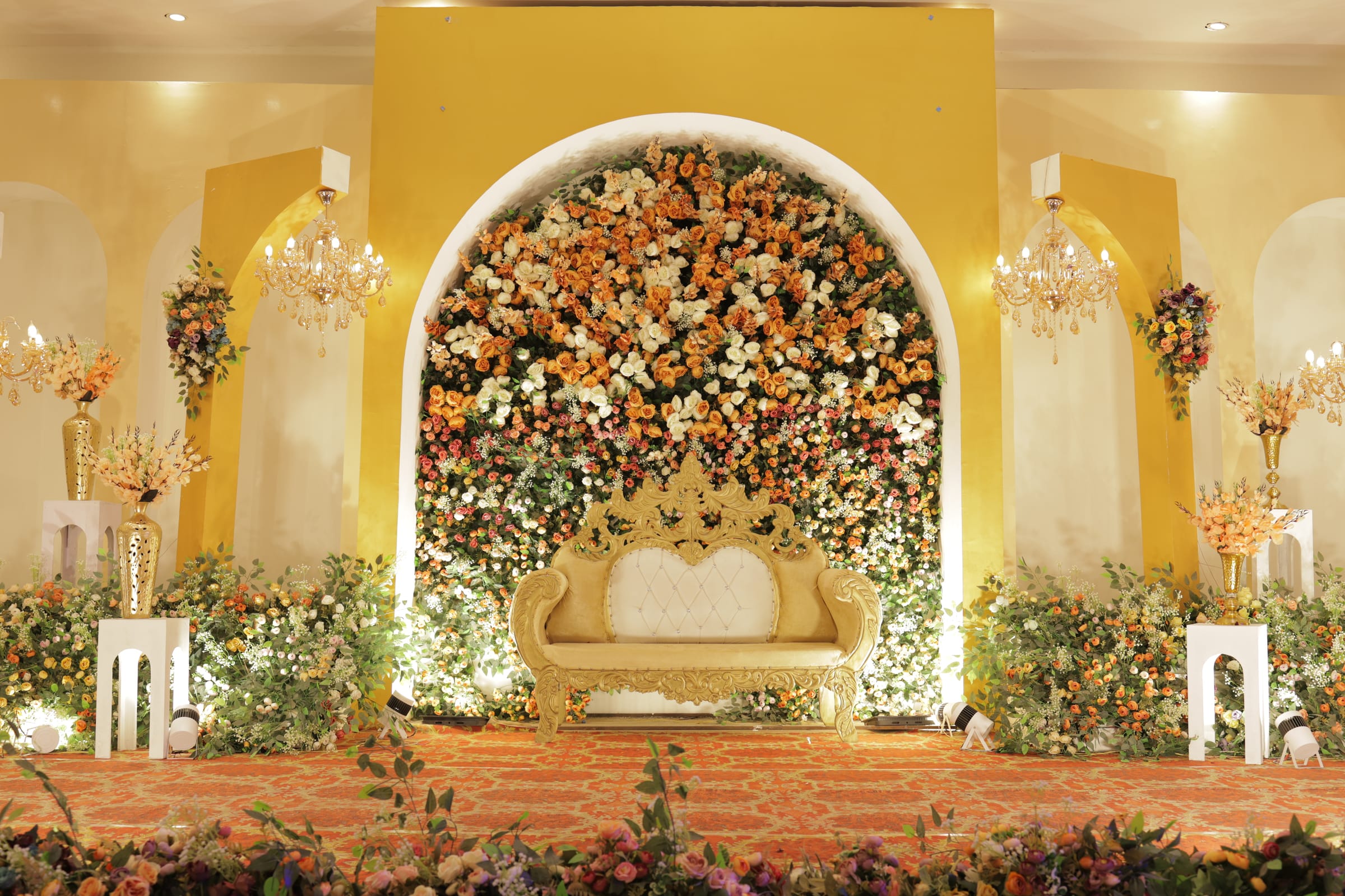 A marigold and rose floral arch above the wedding sofa